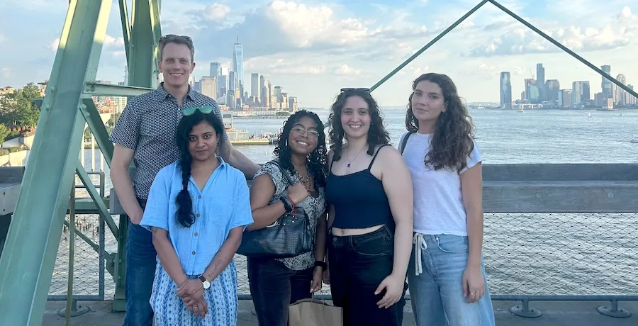 Five people pose for a photo with the Hudson River and lower Manattan skyline in the background. 